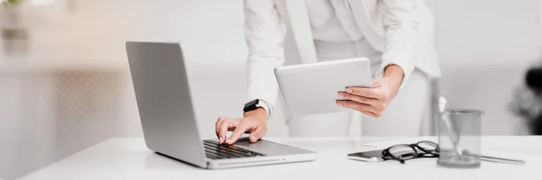 Zahnärztin hat ein Tablet in der Hand während sie den Laptop bedient.