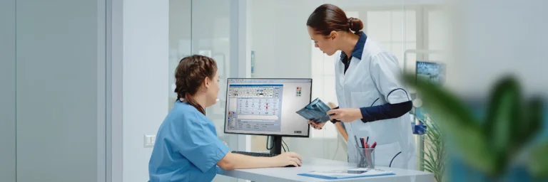 Zahnmedizinische Fachangestellte und Zahnärztin schauen gemeinsam auf die Patientenakte eines Patienten auf dem Computer anschauen.