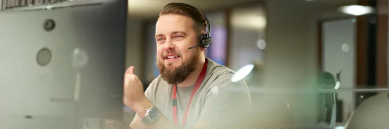 Mitarbeiter aus dem Kundenservice mit einem Headset vor dem Computer.