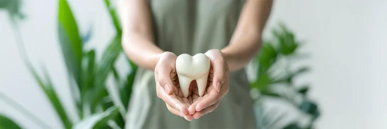 Frau hält symbolisch einen Zahn in der Hand. Im Hintergrund befinden sich Pflanzen.